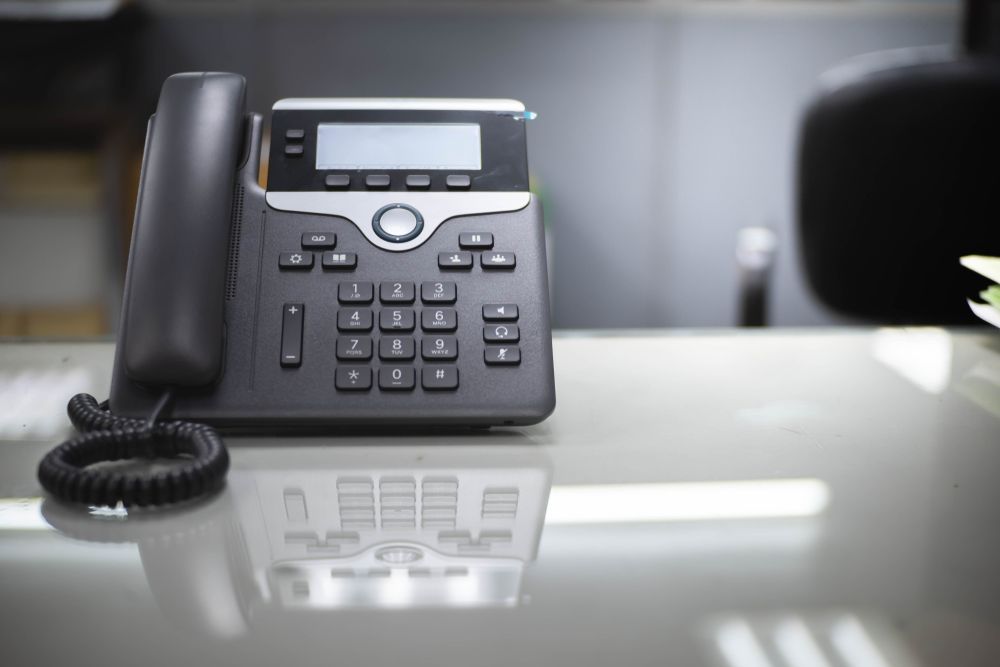 Black Office Desk Phone With Coiled Cord on a Glossy Tabletop — Pacific Telephone & Data In Cessnock, NSW