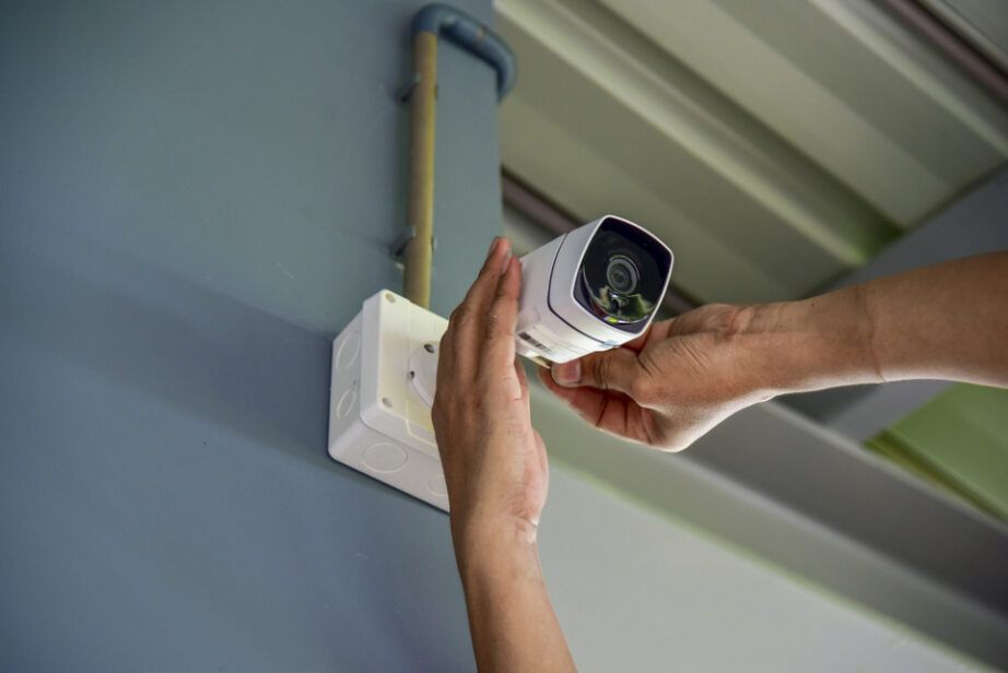 Person Installing a White Security Camera on A Blue Wall — Pacific Telephone & Data in Hunter Valley, NSW