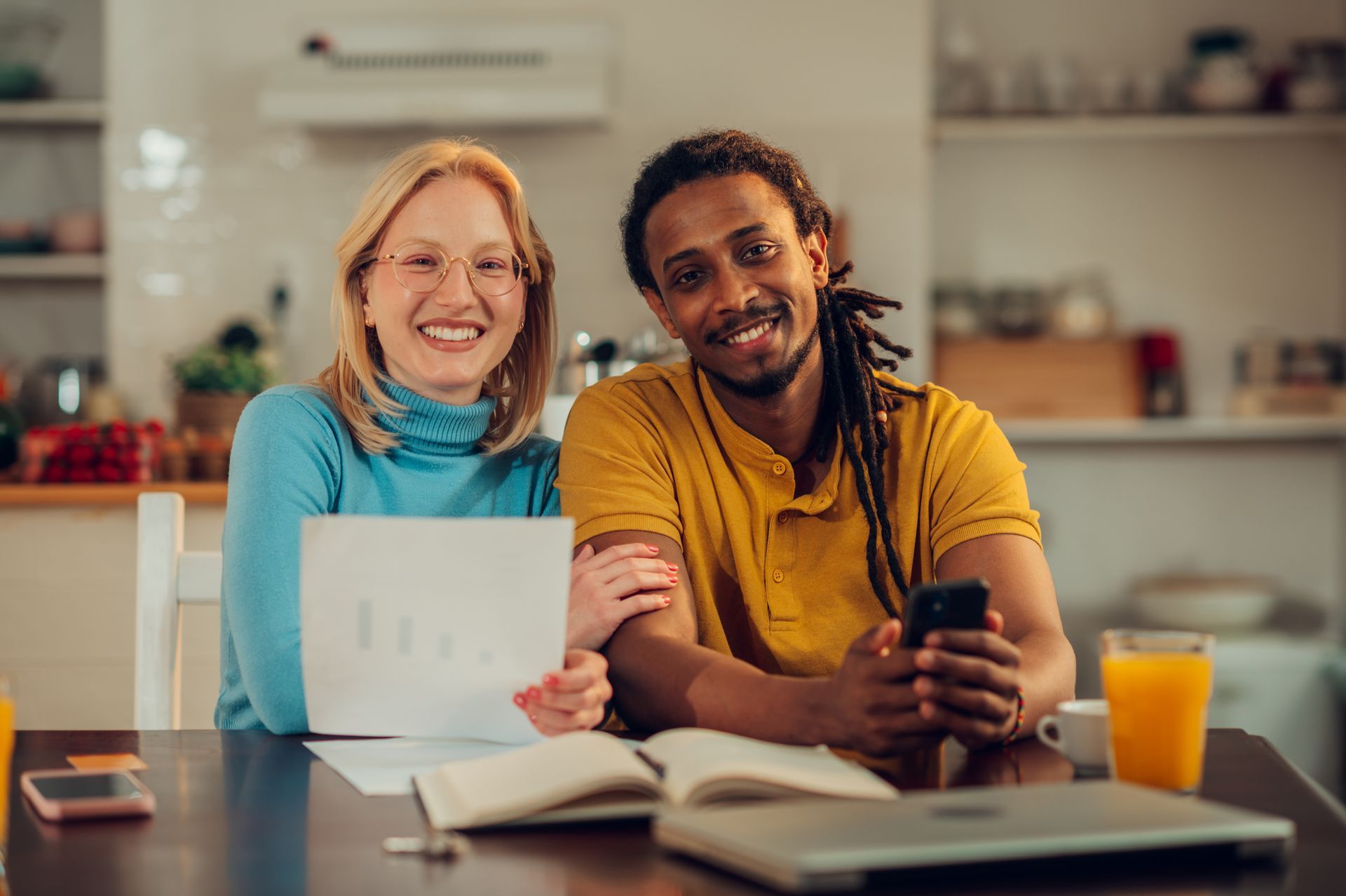 A man and a woman are sitting at a table with a laptop and a cell phone.