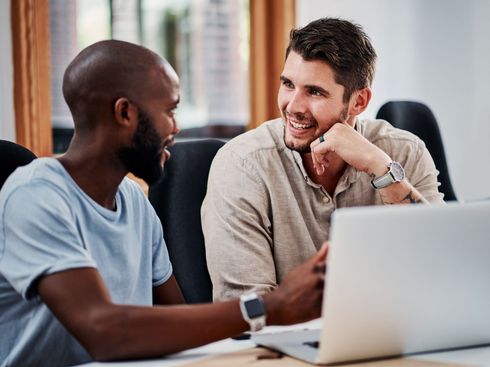 Two men are sitting at a table looking at a laptop computer.