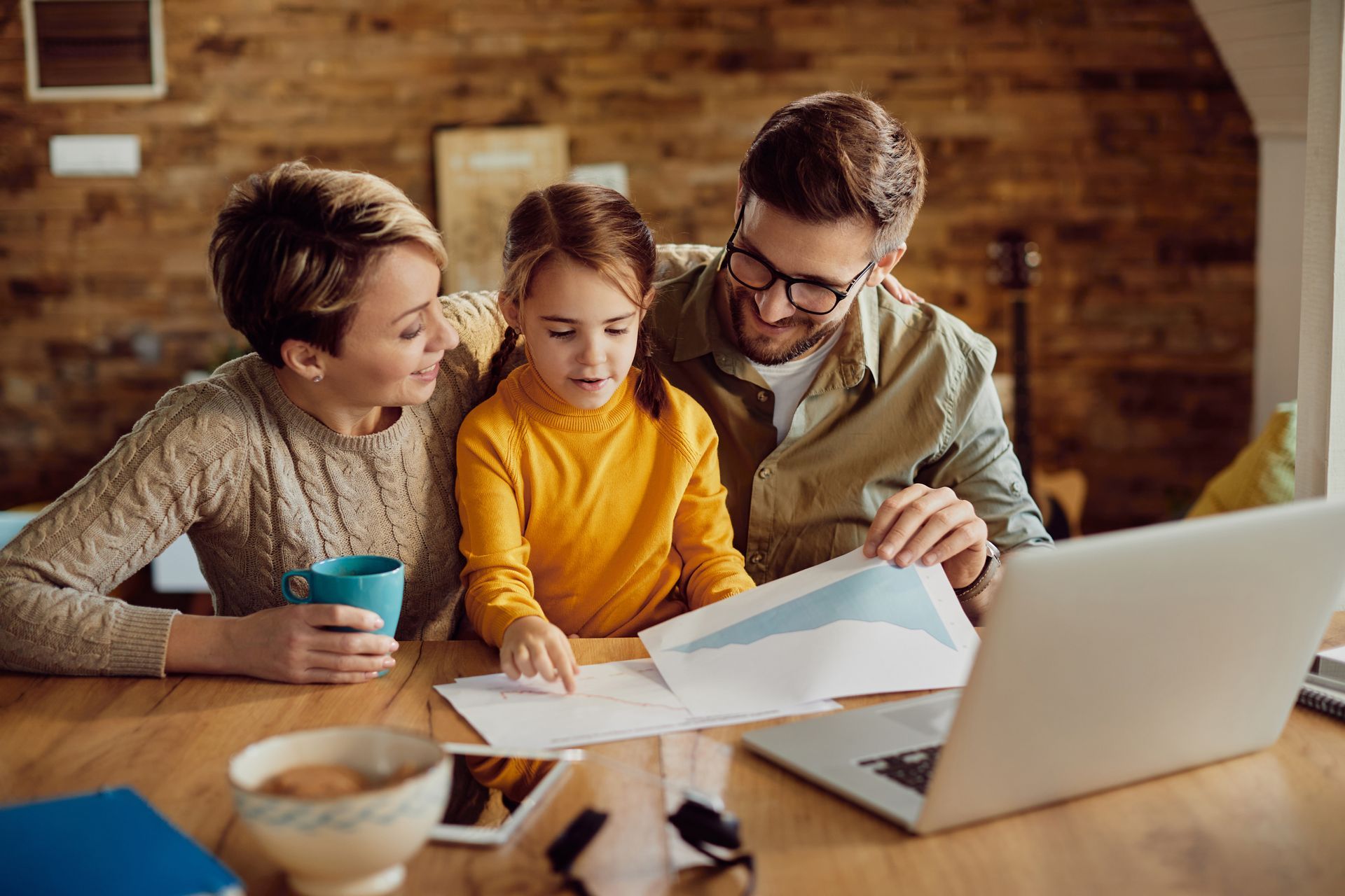 A family is sitting at a table looking at a laptop computer.