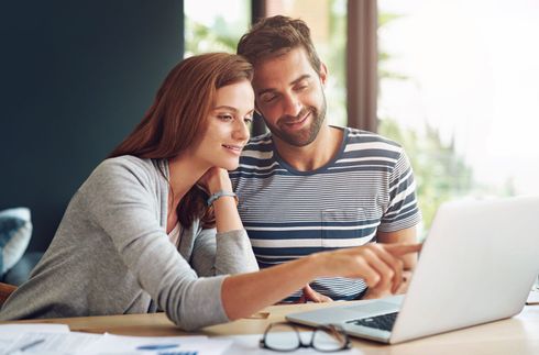 A man and a woman are sitting at a table looking at a laptop computer.