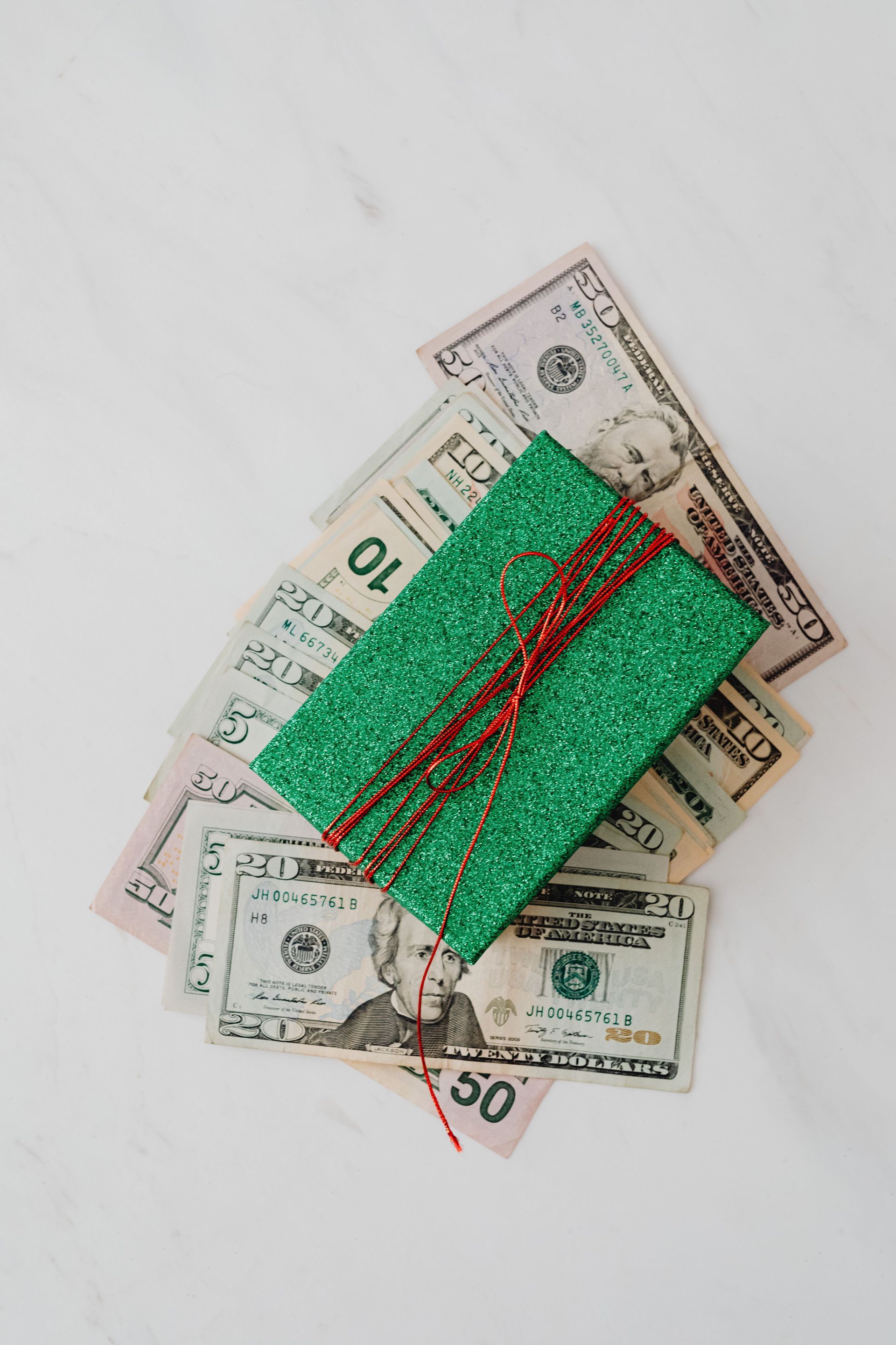 Green gift box tied with red ribbon on scattered U.S. dollar bills on a white surface