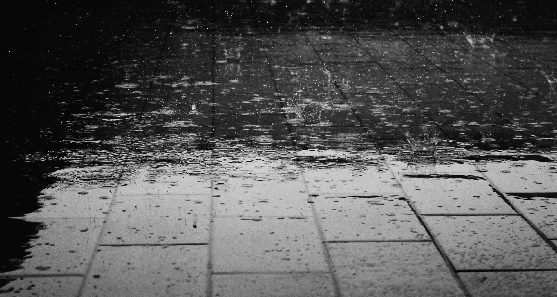 A black and white photo of rain falling on a tiled floor