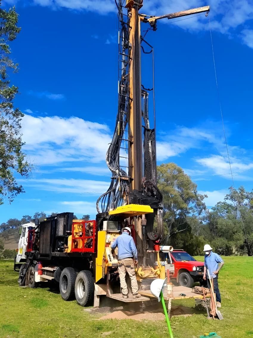 Drilling Rig on a Truck in a Grassy Field With Two Workers — Local Drilling Services In Kingaroy, QLD