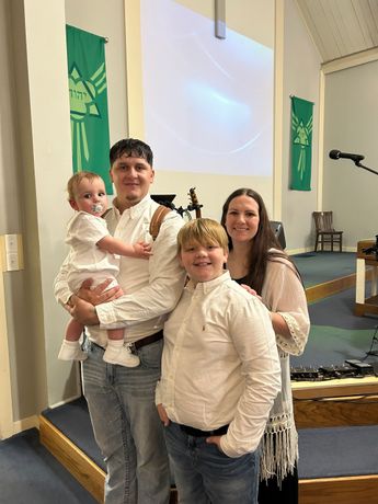 Family posing on a church stage, with green banners and a projection screen behind them.