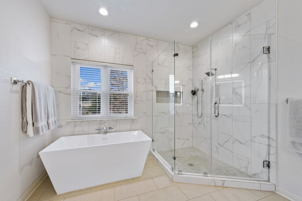 Modern white bathroom with freestanding tub, glass shower, and window shutters