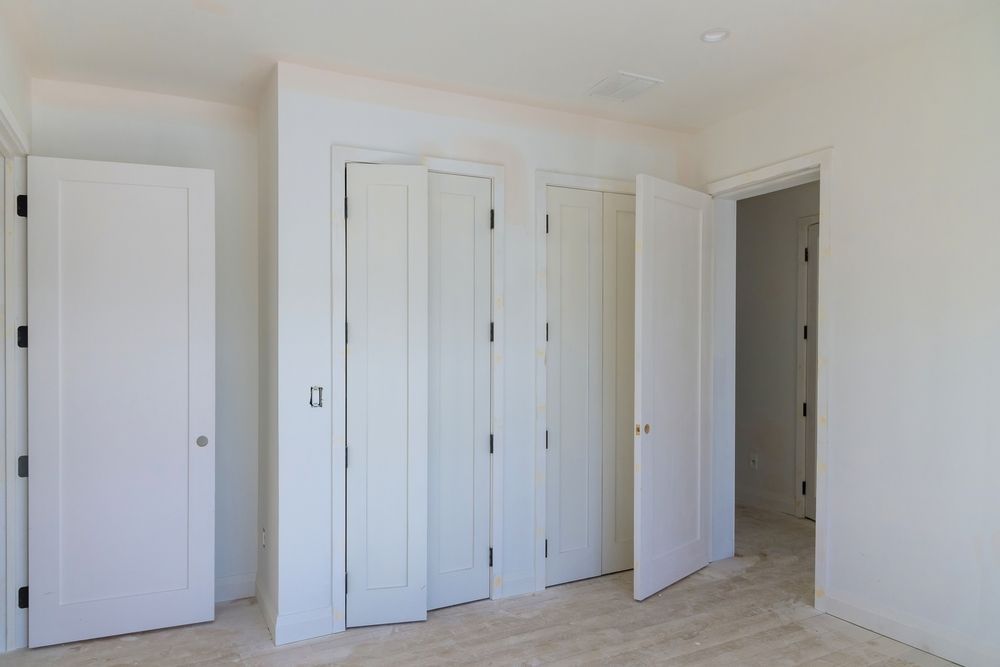 Empty white bedroom with multiple doors and light wood flooring