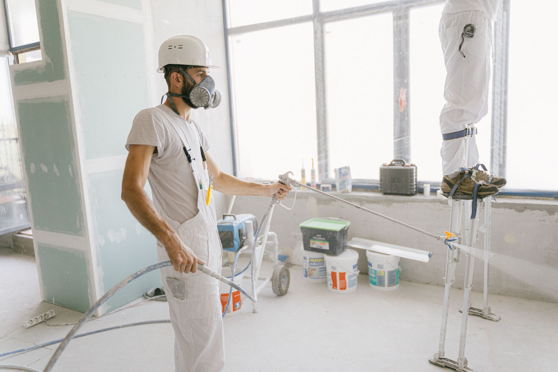 Worker in white protective gear and mask painting a bright room with a roller