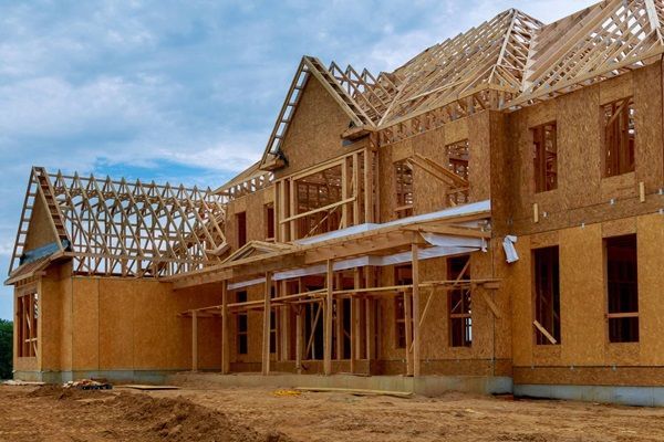 Wood-framed house under construction with exposed roof trusses and unfinished exterior walls