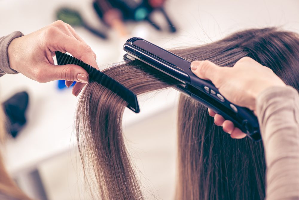 Hands Using a Comb and a Flat Iron to Straighten Long — Oh So Blonde Hair Studio in Buddina, QLD
