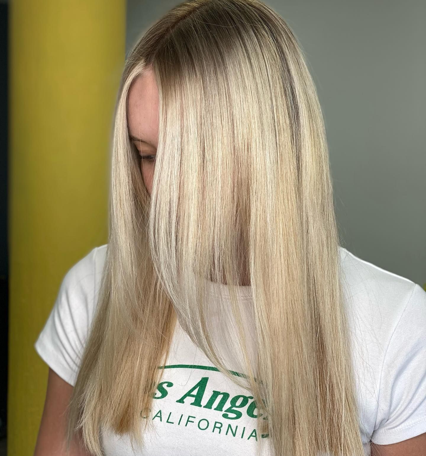 Person With Long Straight Blonde Hair Covering Their Face, Wearing A White T-shirt Against A Muted Green Background — Oh So Blonde Hair Studio in Kawana, QLD