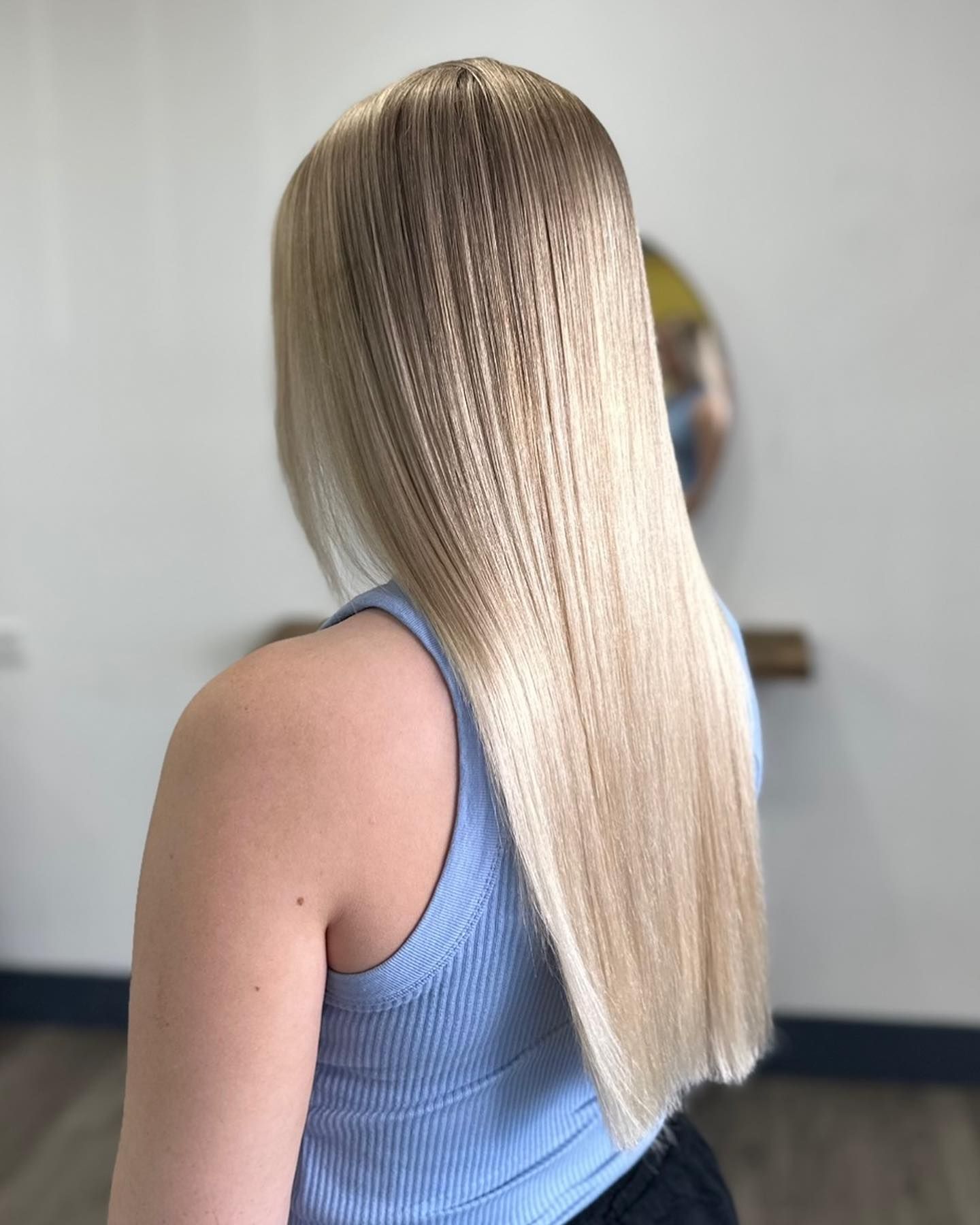 Woman With Long Straight Blonde Hair In A Blue Sleeveless Top, Viewed From Behind In A Salon Setting — Oh So Blonde Hair Studio in Kawana, QLD