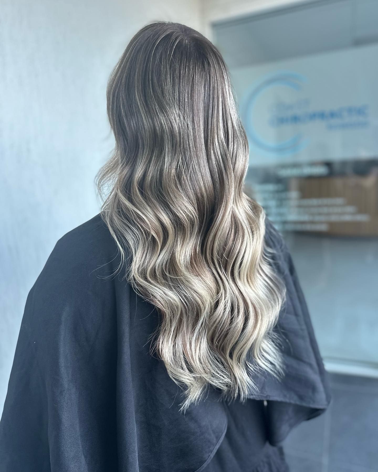 Back View Of Long Wavy Blonde Hair On A Person In A Black Top Indoors — Oh So Blonde Hair Studio in Kawana, QLD