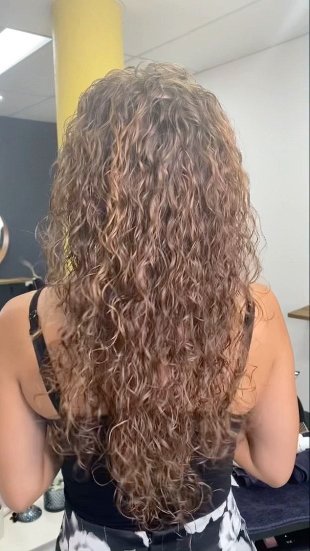Person Seen From Behind With Long Curly Brown Hair, Wearing A Black Top In A Bright Indoor Room — Oh So Blonde Hair Studio in Kawana, QLD