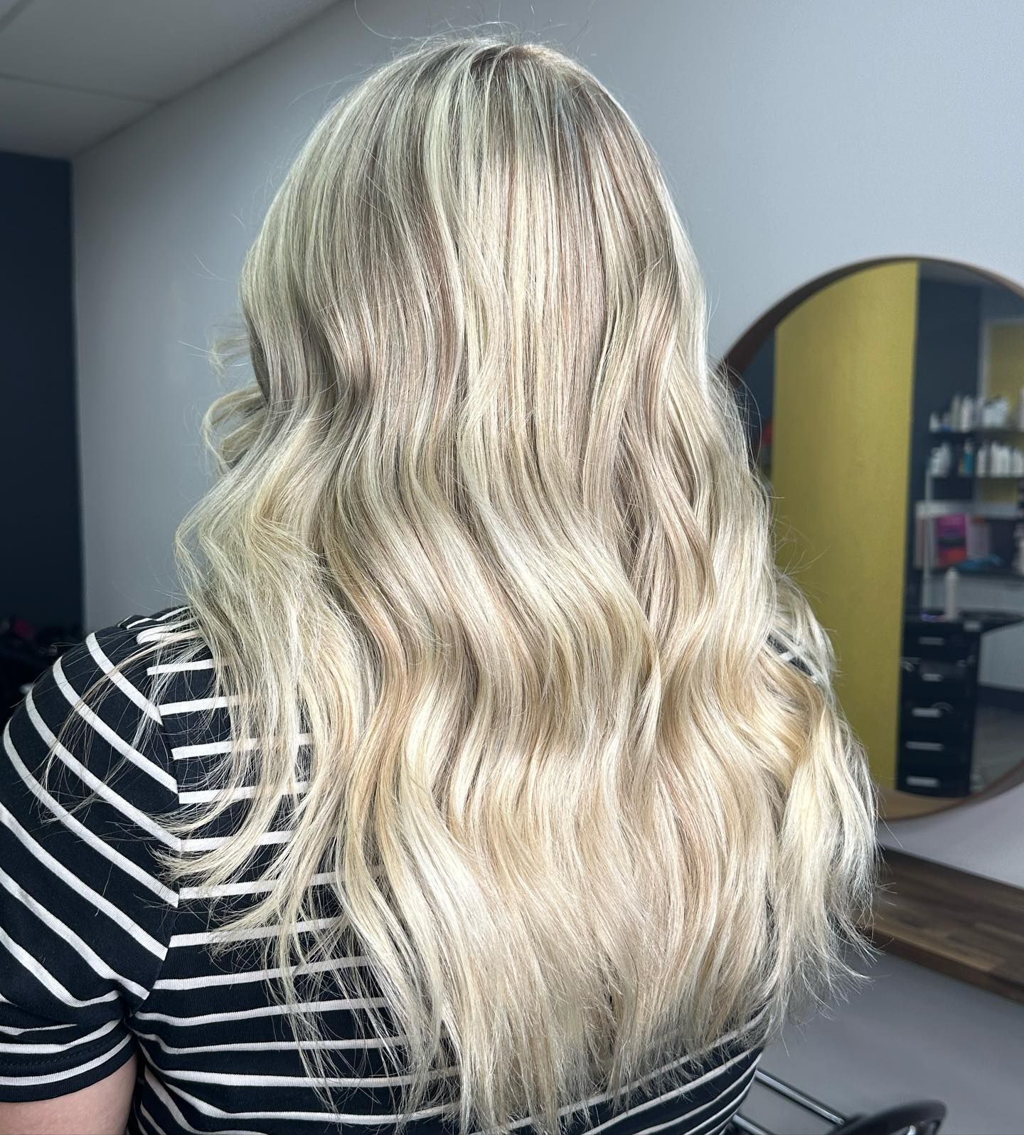 Back View Of Long Wavy Blonde Hair With Dark Roots Against A Mirror And Salon-like Interior — Oh So Blonde Hair Studio in Kawana, QLD