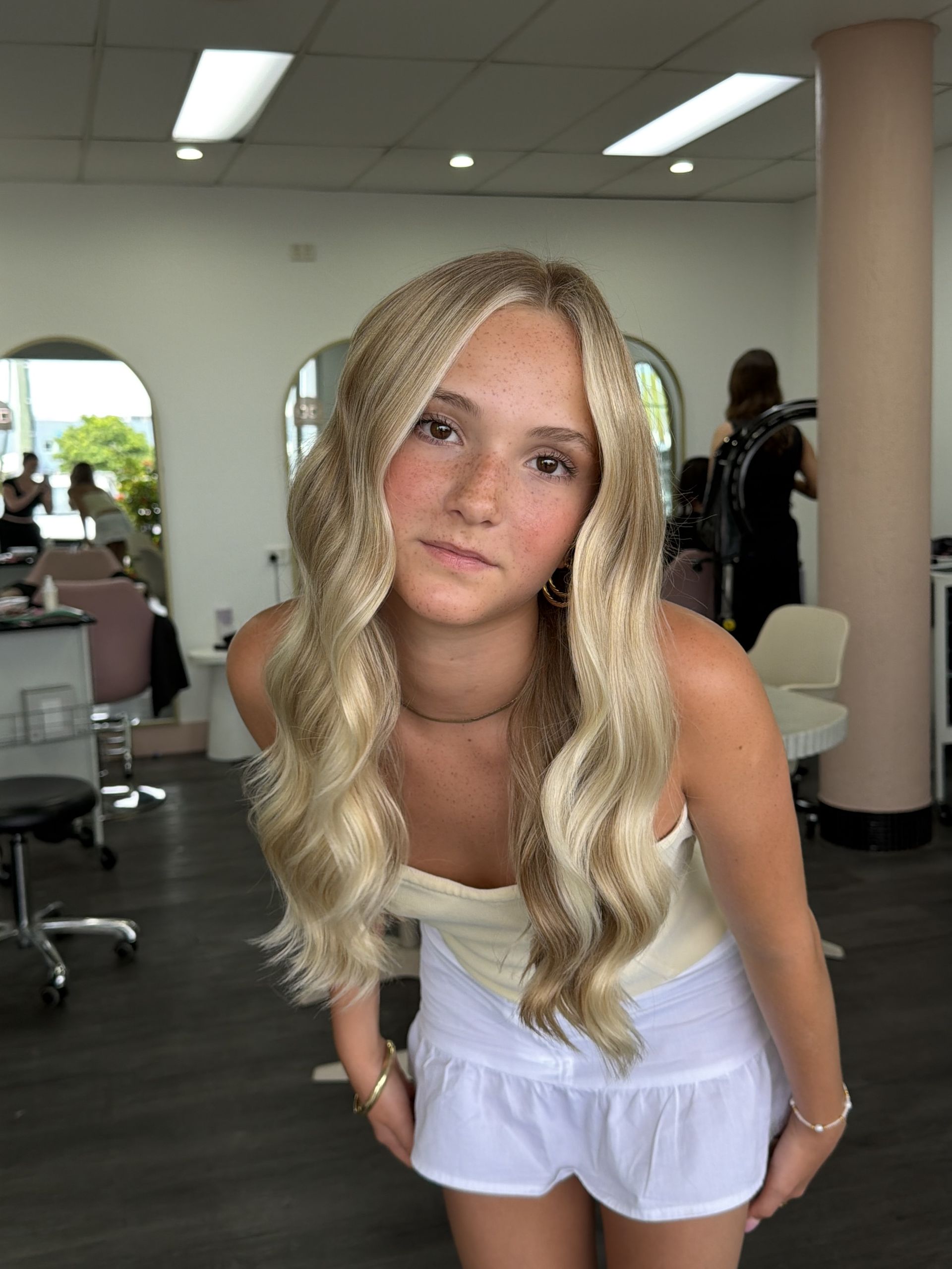 Person With Long Blonde Hair Posing In A Salon, Wearing A White Tank Top And Light Lavender Shorts — Oh So Blonde Hair Studio in Kawana, QLD