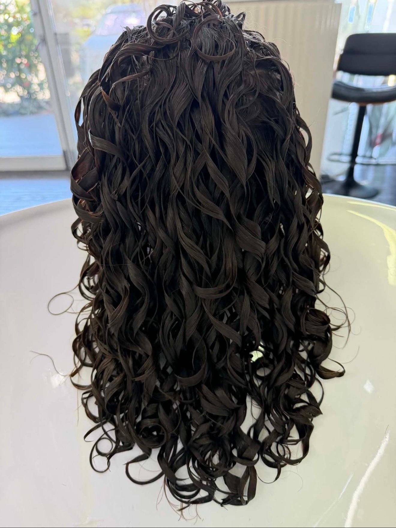 Back View Of Dark Curly Hair In A Salon Chair With A Bright Window In The Background — Oh So Blonde Hair Studio in Kawana, QLD