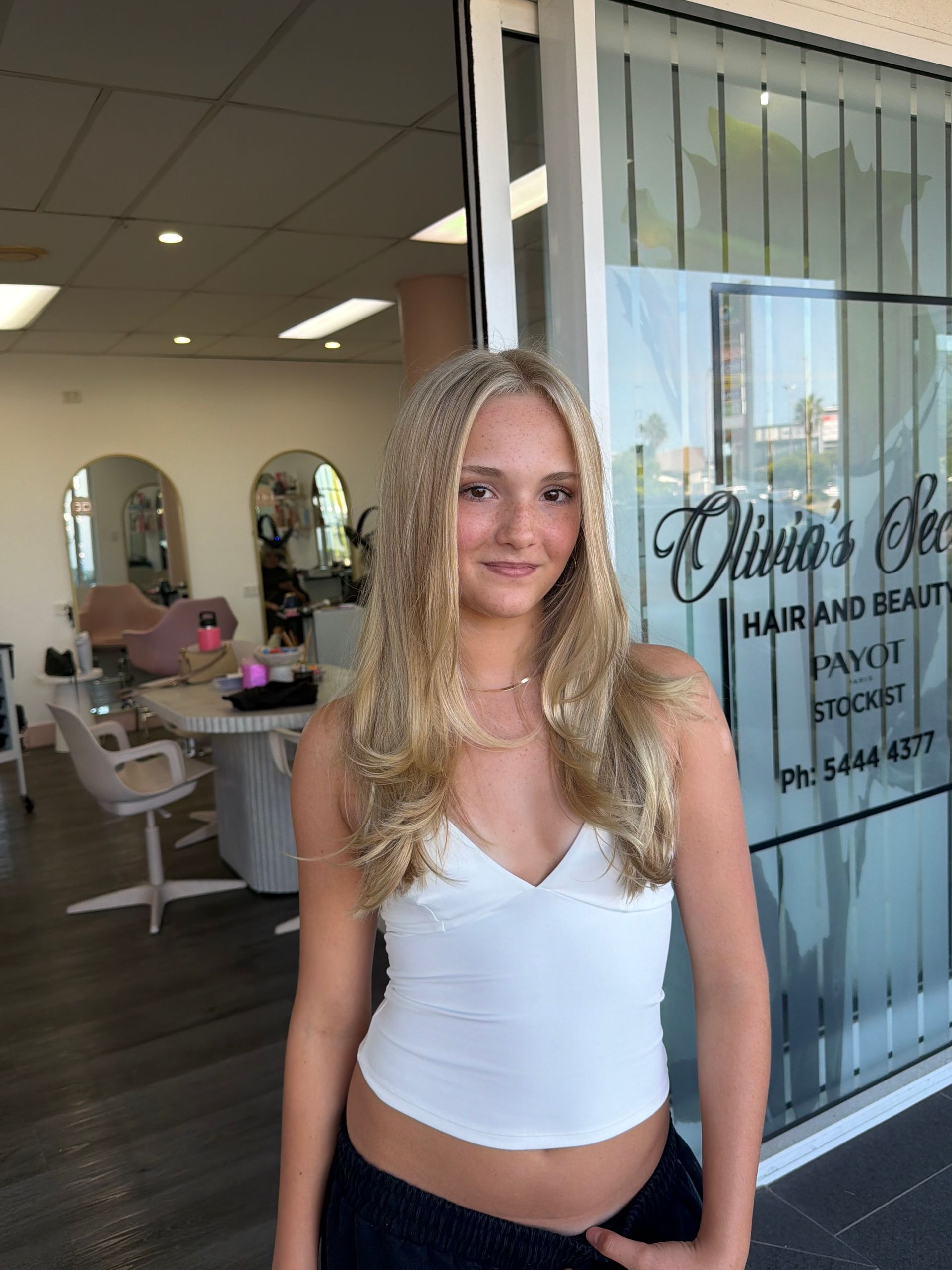 Woman Standing In A Salon Entrance, Wearing A White Top And Smiling Softly — Oh So Blonde Hair Studio in Kawana, QLD