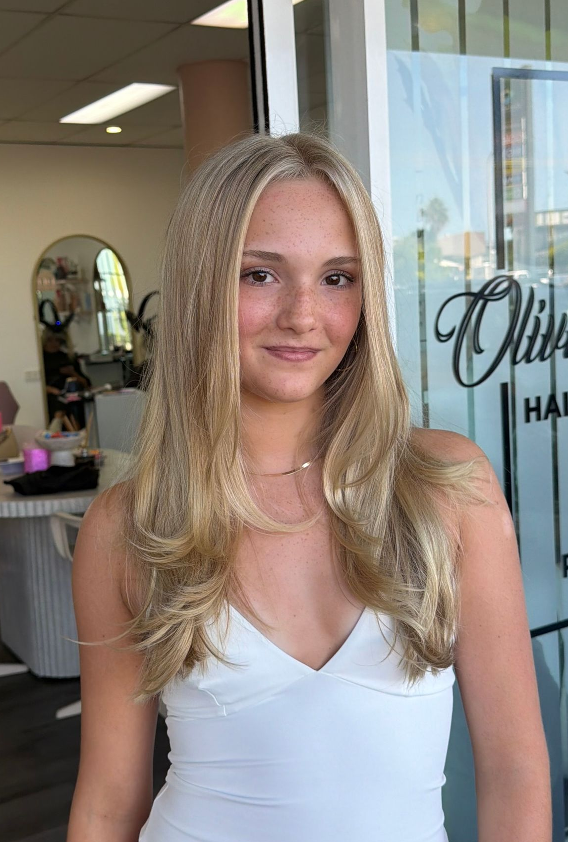 Smiling Woman In A White Dress Standing Indoors Near A Salon Window — Oh So Blonde Hair Studio in Kawana, QLD