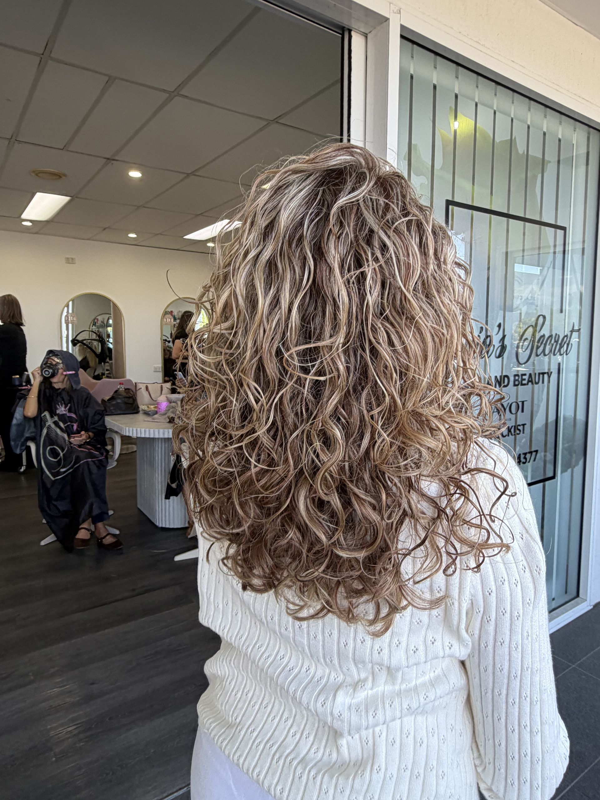 Woman With Curly Hair In A White Sweater Standing In A Salon, Viewed From Behind — Oh So Blonde Hair Studio in Kawana, QLD