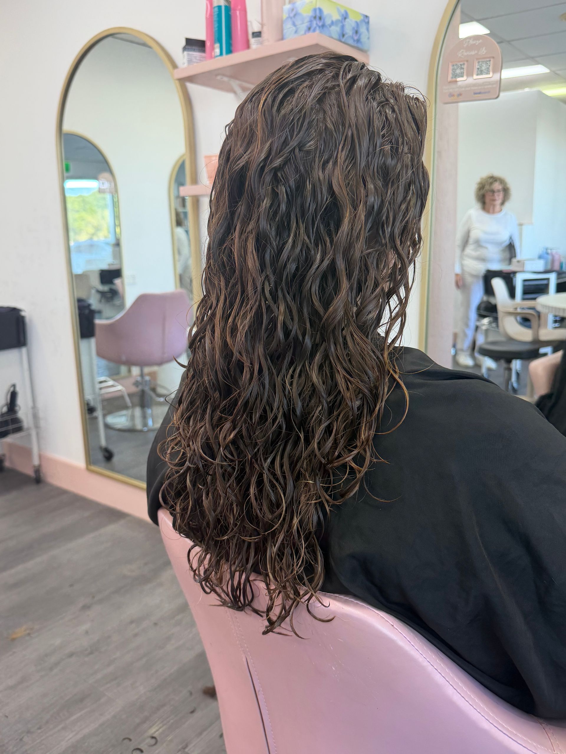 Woman With Wet Curly Hair Sitting In A Salon Chair, Seen From Behind, With Mirrors And Styling Stations In The Background — Oh So Blonde Hair Studio in Kawana, QLD