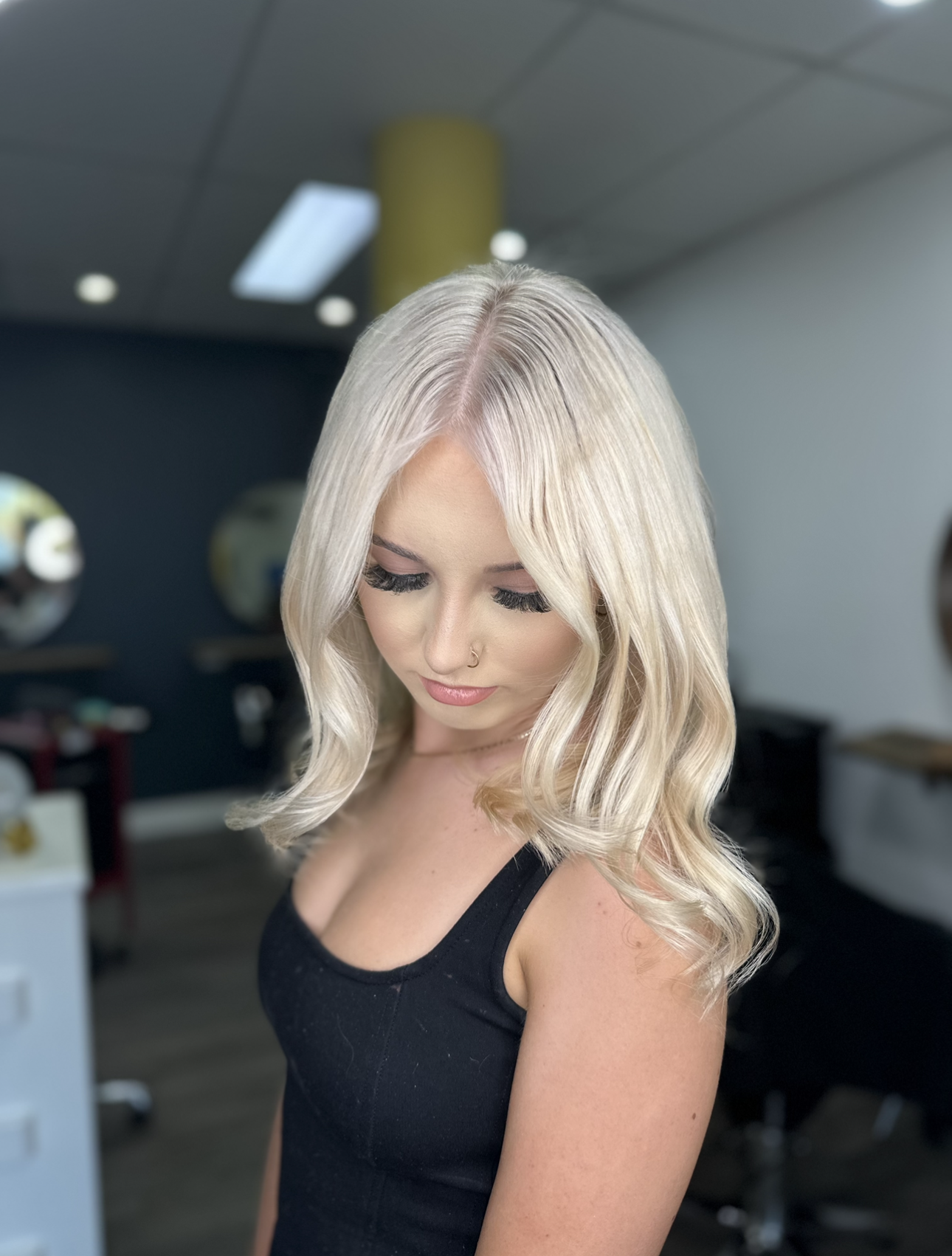 Blonde Woman With Wavy Hair In A Black Top, Looking Down In A Salon Interior — Oh So Blonde Hair Studio in Kawana, QLD