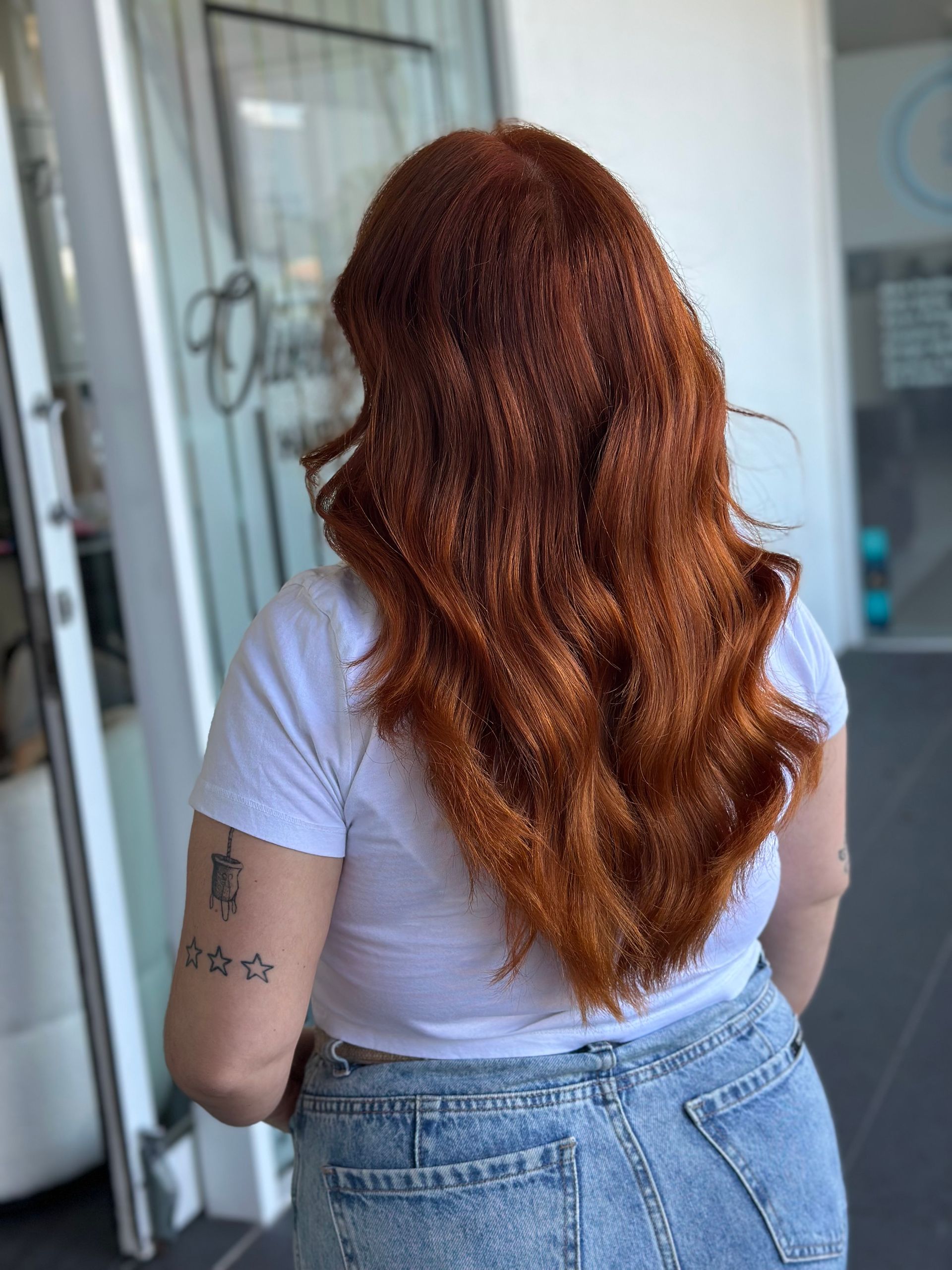 Person With Long Curly Auburn Hair In A White Shirt And Jeans, Seen From Behind In A Doorway — Oh So Blonde Hair Studio in Kawana, QLD