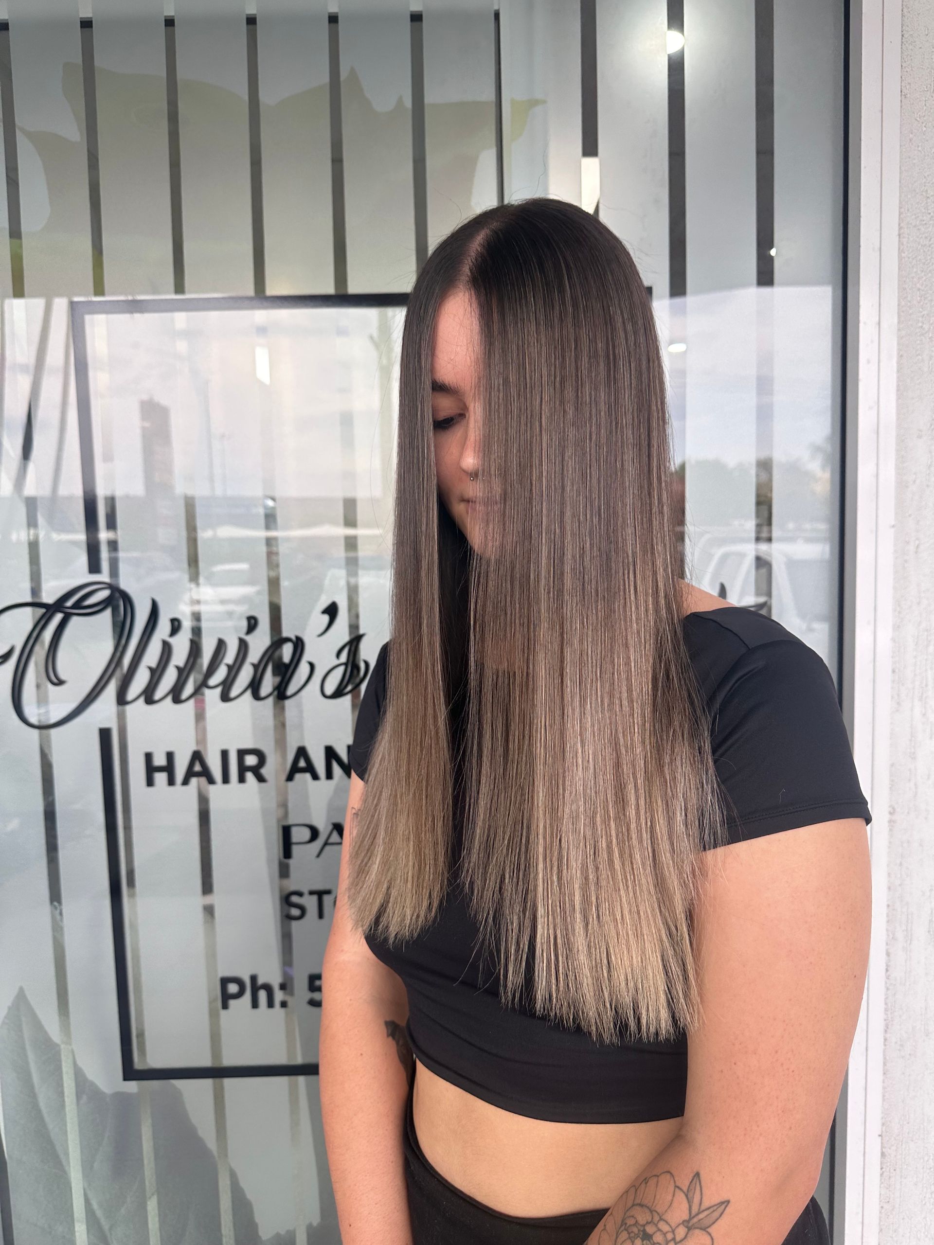 Woman With Long Straight Hair Standing Outside A Salon Window, Wearing A Black Crop Top And Pants — Oh So Blonde Hair Studio in Kawana, QLD