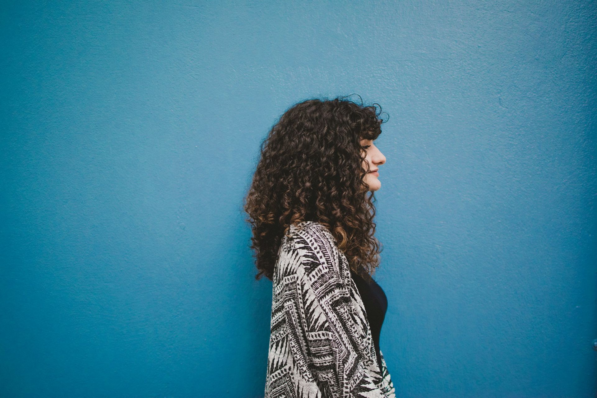 Woman With Curly Brown Hair Wearing a Patterned Jacket — Oh So Blonde Hair Studio in Buddina, QLD