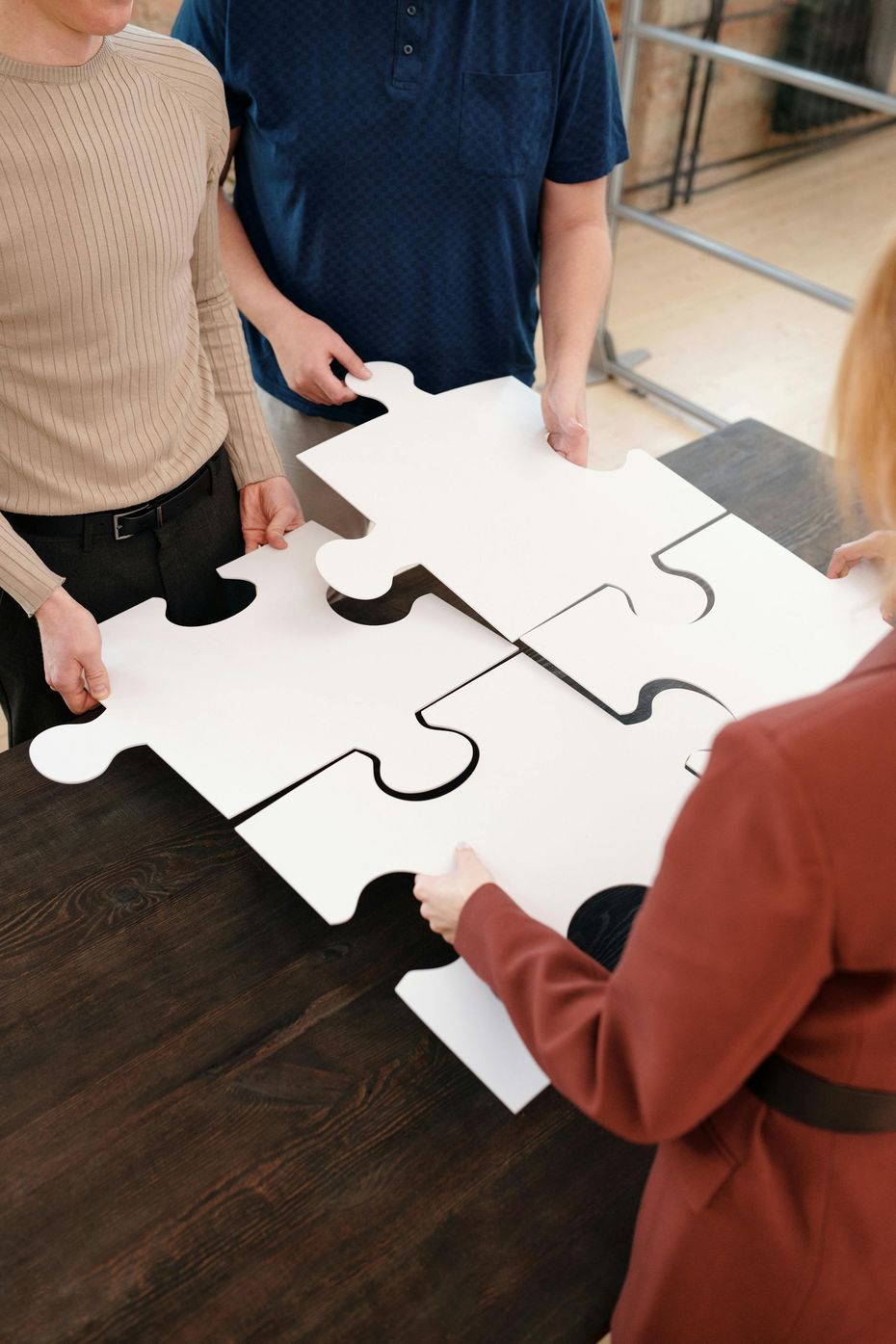 People assembling a large white jigsaw puzzle on a dark table in a classroom or workshop