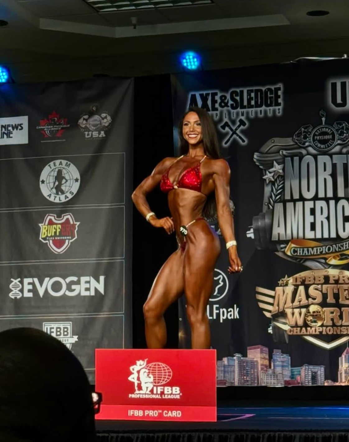 Woman in a red and blue bikini poses on stage at a bodybuilding competition.