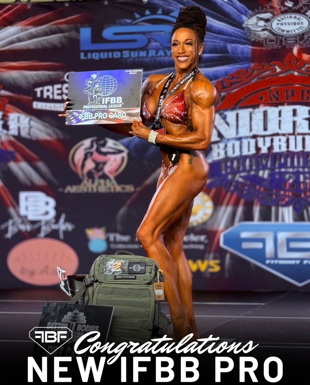 Female bodybuilder posing onstage, holding trophy. Wearing a red and black bikini, flexing muscles.