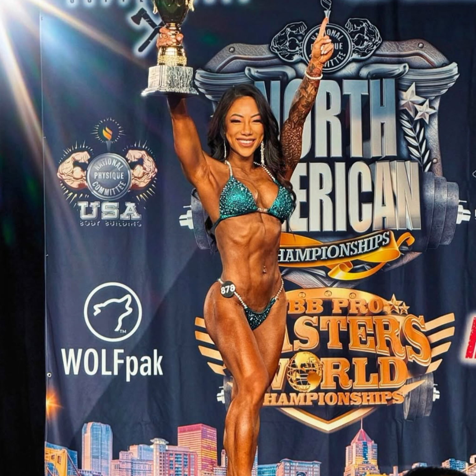 Bodybuilder in teal bikini holding trophy at North American Championships.