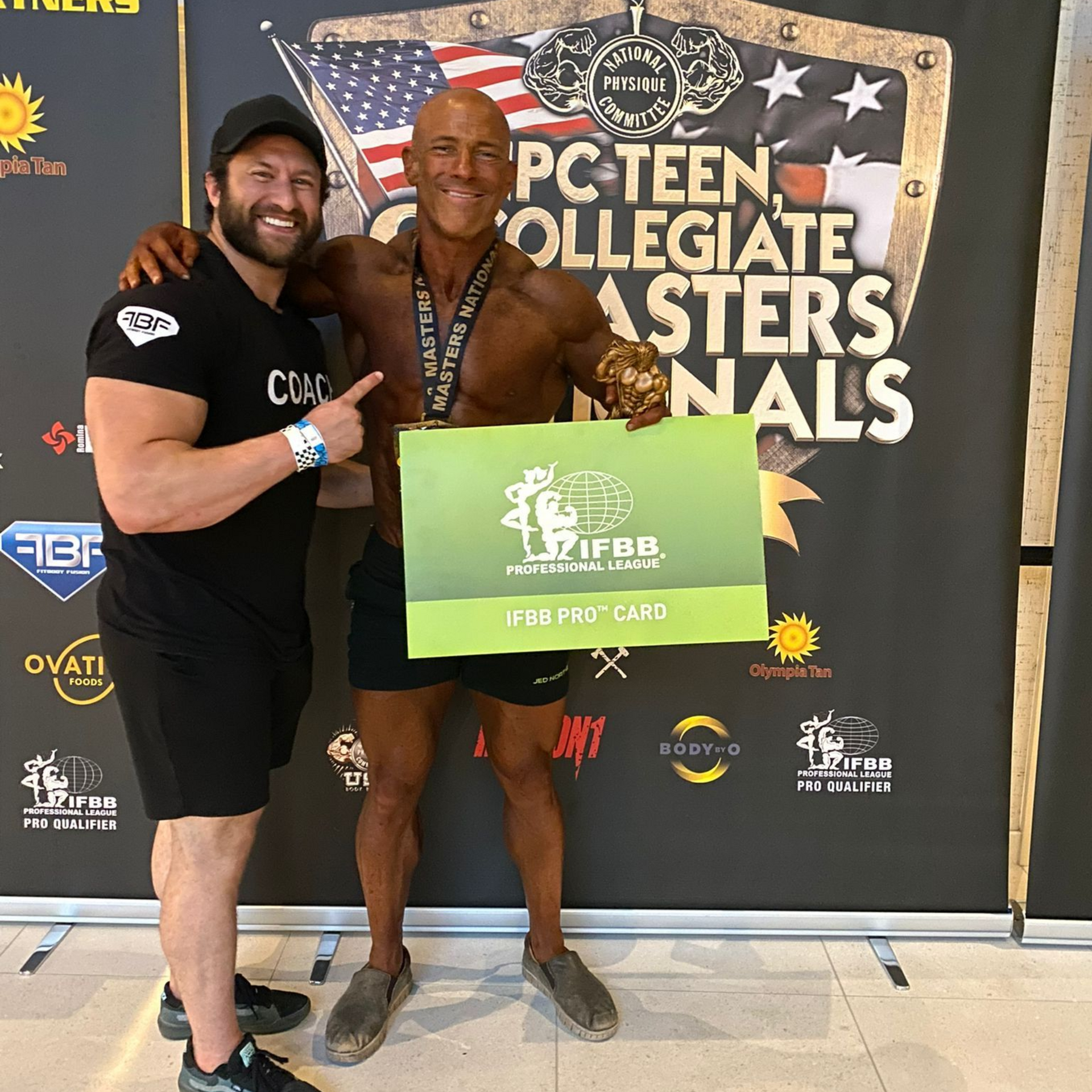 Man with coach holding pro card after competition; stage backdrop.