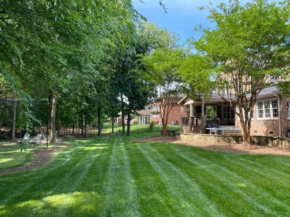 A lush green lawn in front of a house surrounded by trees.