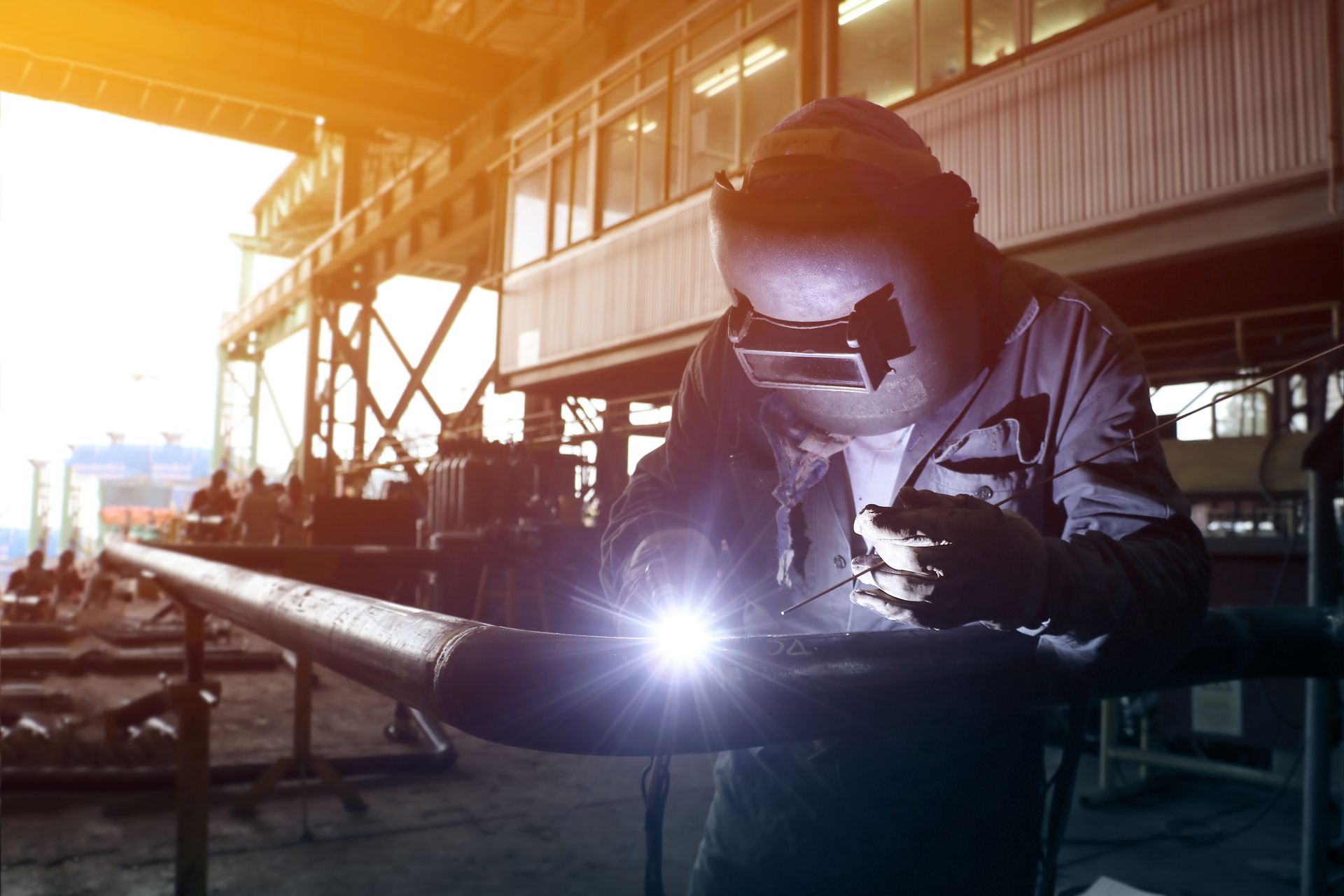 A man wearing a welding mask is welding a pipe in a factory.