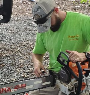 Person in green shirt using a chainsaw on a log outdoors.
