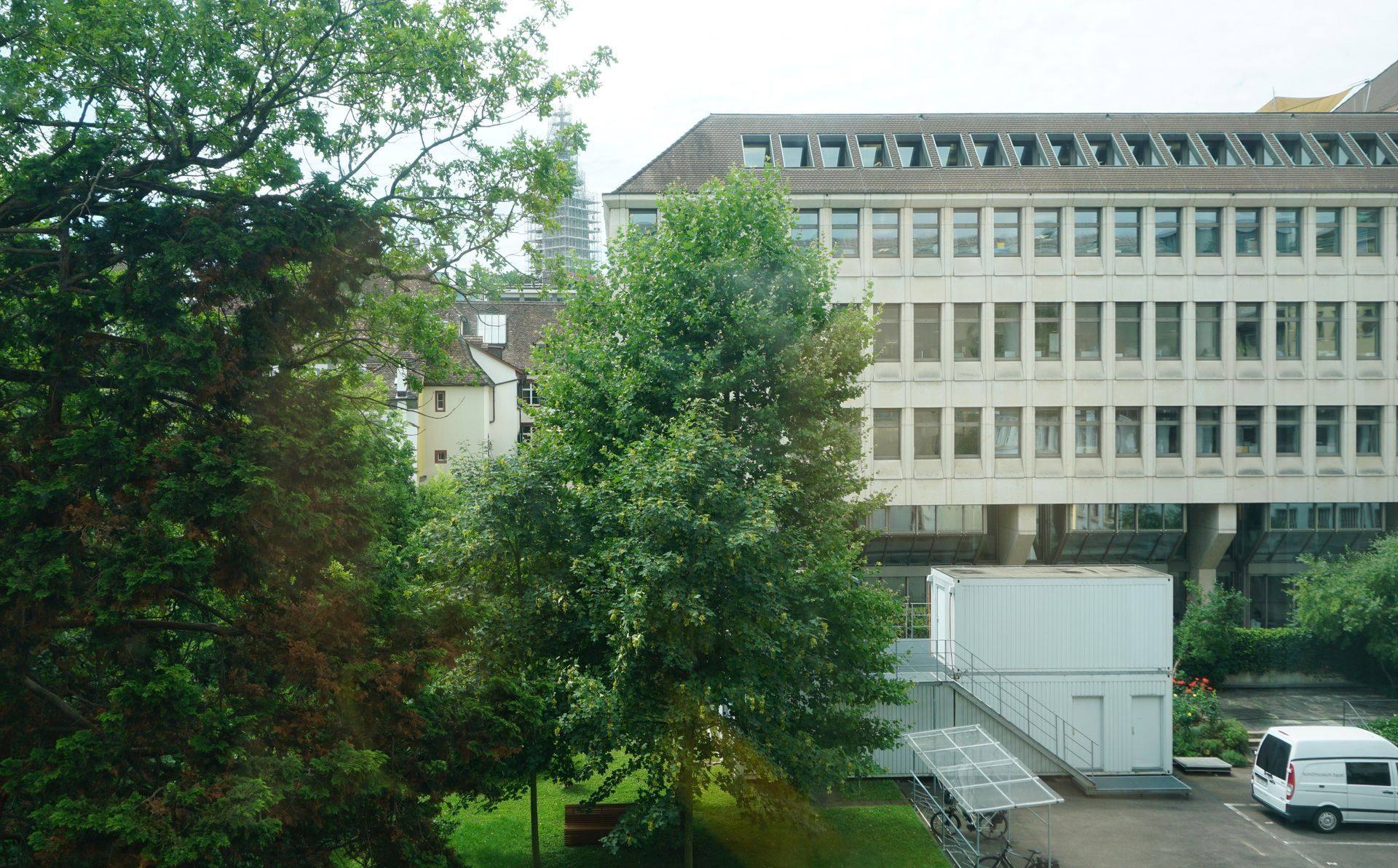 Tree-lined view of a beige office building with many windows and parked vehicles below