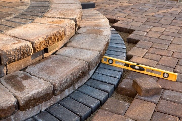 Level on curved stone paving beside stacked curb blocks and a brick patio