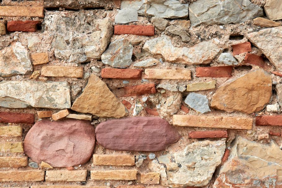 Close-up of a rough stone and brick wall with tan, red, and pink stones.