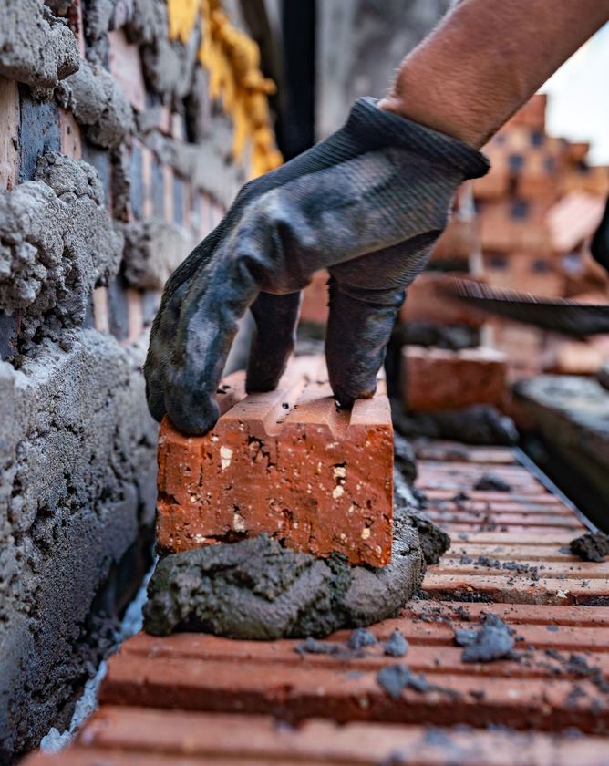 Gloved hand placing a red brick with mortar on a construction wall