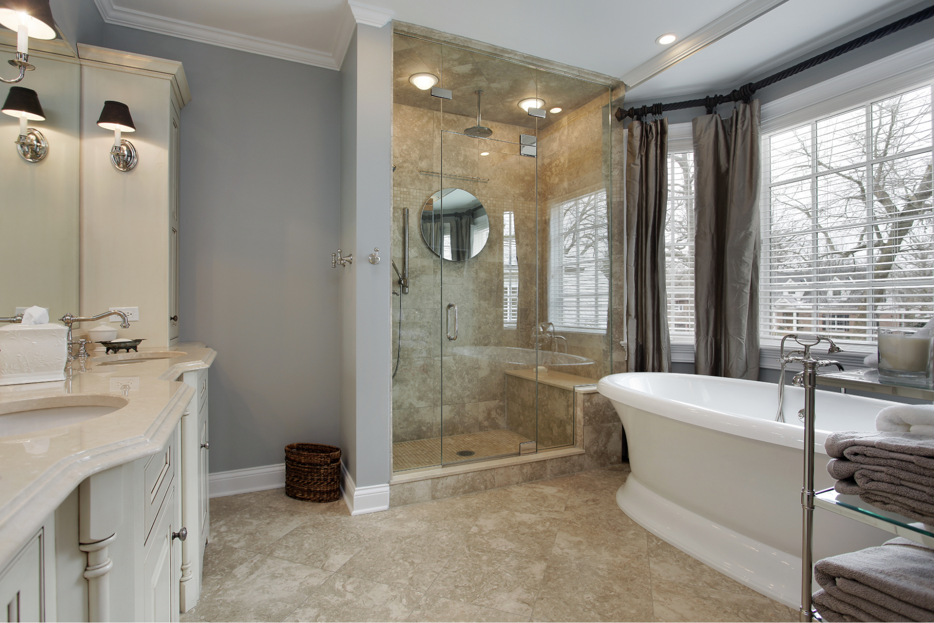 Elegant bathroom with glass shower, bathtub, and large window with curtains.