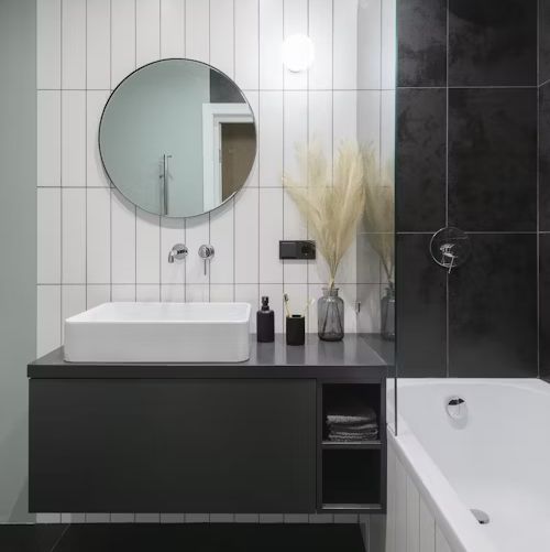 Modern bathroom with black and white tile, floating vanity, round mirror, and bathtub.