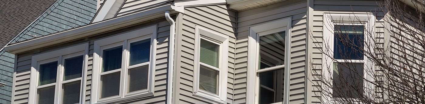 Exterior view of a house with light gray siding and several windows.