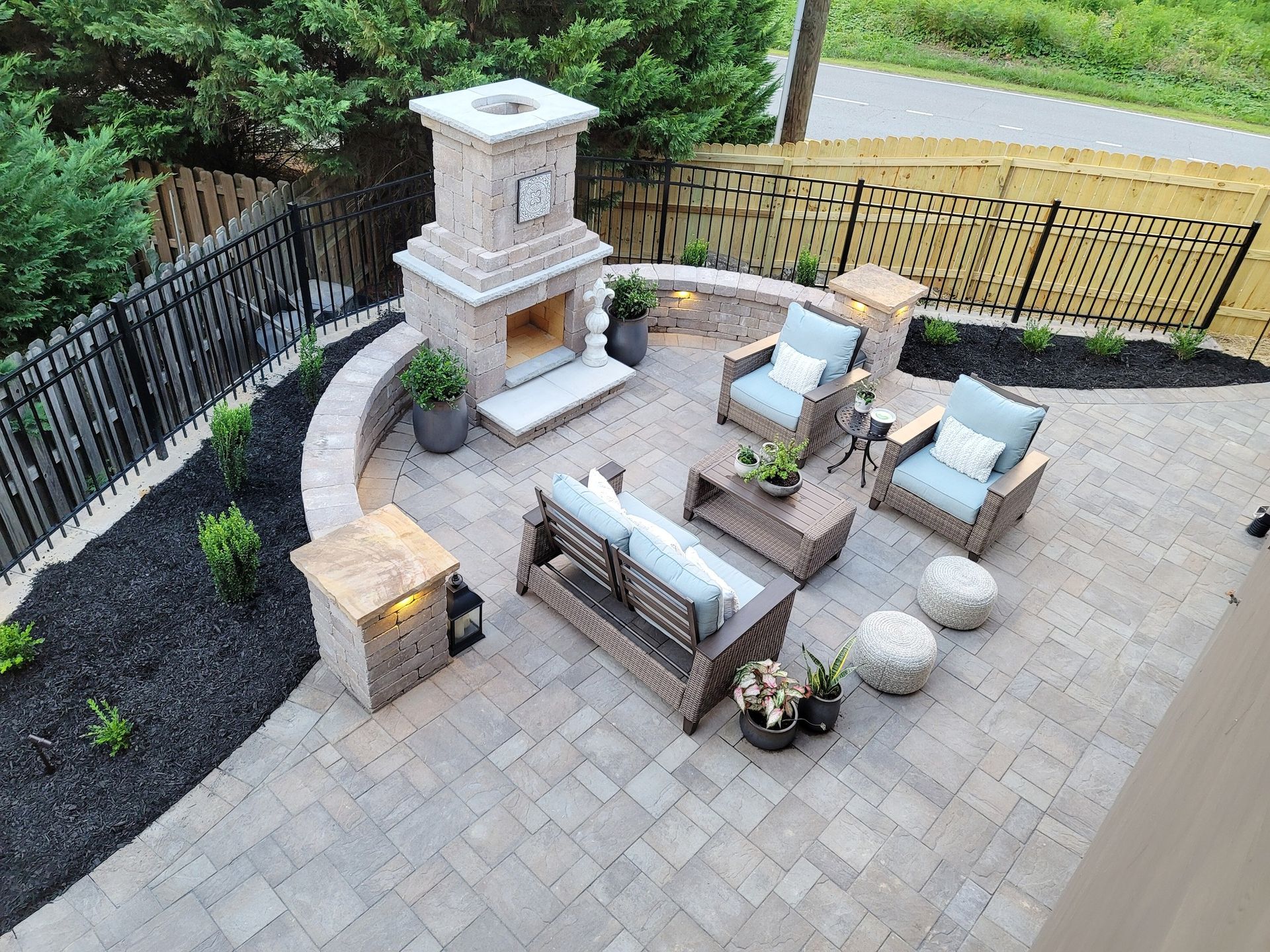 Backyard patio with stone pavers, outdoor seating, fire pit, and built-in grill area surrounded by greenery