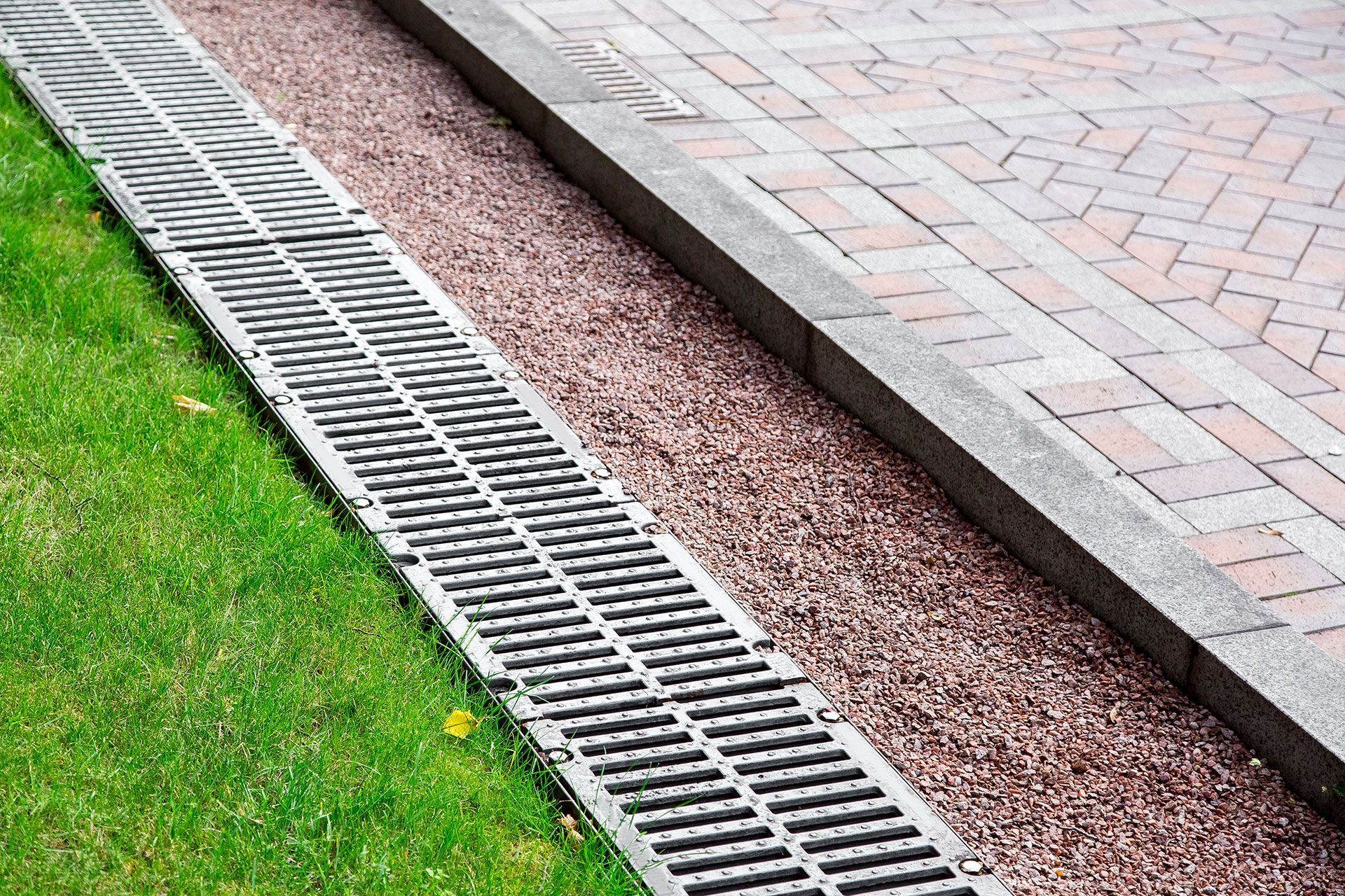Rain gutter drain beside a grassy lawn and paved walkway with gravel border