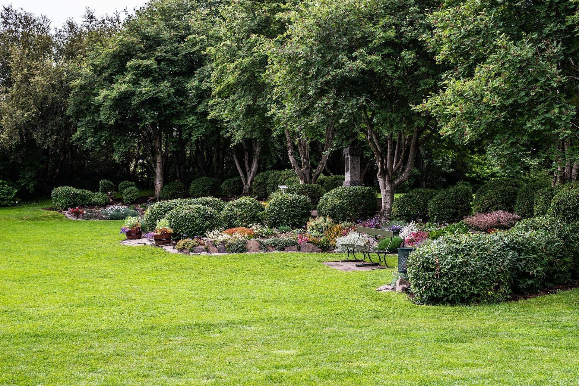Lush green park lawn with flower beds and dense trees in the background