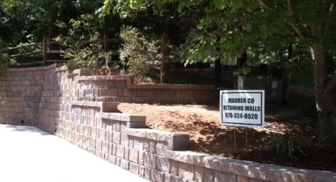 Stone retaining wall with a white sign in front of trees and shrubs outdoors