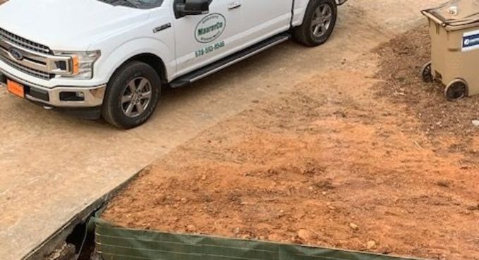 White utility truck parked on a dirt lot beside a concrete edge and tan trash bin.